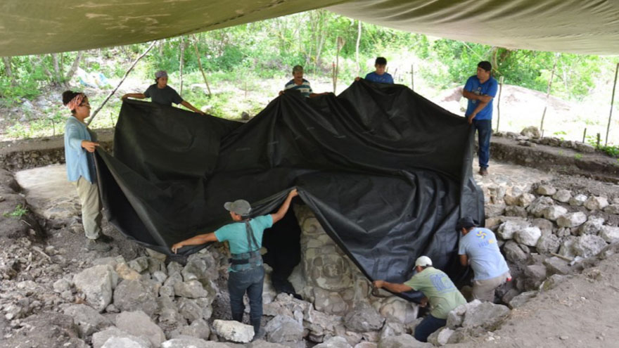 Archaeologists and workers protect the now excavated mask from the elements using tarps and a tent. Photo: INAH
